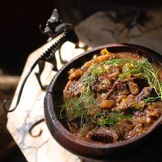 a wooden bowl filled with meat and vegetables on top of a marble table next to a metal faucet