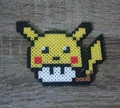 a piece of art made out of perler beads on a wooden surface, with an image of a pikachu