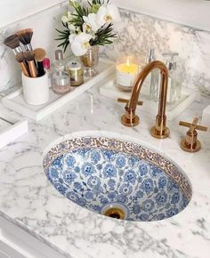 a bathroom sink with marble counter top and gold faucet, surrounded by white flowers