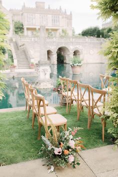 an outdoor ceremony setup with wooden chairs and flowers on the grass in front of a pond