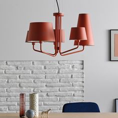 a dining room table and chairs with pink lamps hanging from the ceiling over it, in front of a white brick wall