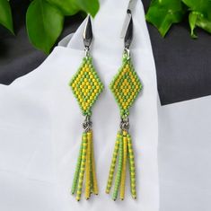 a pair of yellow and green beaded earrings on top of a white cloth next to plants