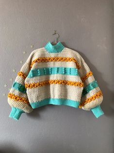 a sweater hanging on the wall with stars around it and an orange, white, and blue stripe pattern