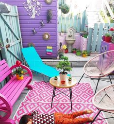 an outdoor patio with colorful furniture and potted plants on the floor, in front of a purple wall