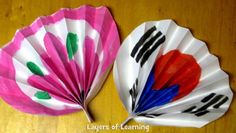 two colorful paper fans sitting on top of a wooden table with black and red designs