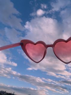 a pair of pink heart shaped sunglasses hanging from the side of a pole with clouds in the background