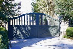 a gated driveway leading to a house with trees in the back ground and bushes on either side