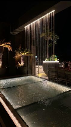 an indoor swimming pool at night with lights on the side and palm trees in the background