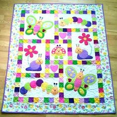 a quilted wall hanging on the floor with many bugs and flowers in different colors