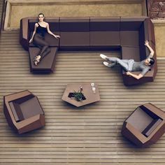 two people sitting on couches and tables in an outdoor area with wood flooring