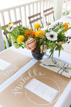 an arrangement of flowers on a table with place cards and napkins for guests to sign