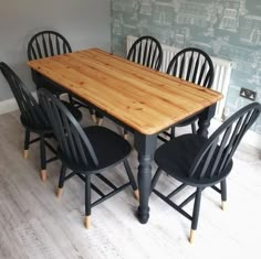 a wooden table surrounded by black chairs in front of a wall with blue and green wallpaper