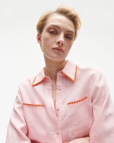 a woman in a pink shirt with an orange trim around her neck and hands folded over her chest