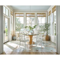 a dining room table surrounded by white chairs and windows with sun shining through the window