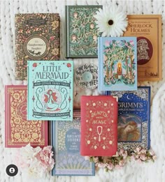 there are many different books on the blanket with flowers in front of them and one has a white daisy