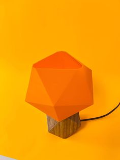 an orange table lamp sitting on top of a wooden stand next to a yellow wall