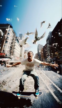 a man riding a skateboard on top of a street next to birds flying around