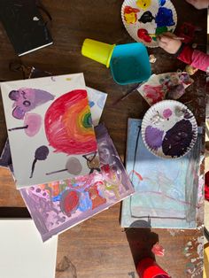 children's artwork and craft supplies on a wooden table with paper plates, scissors, paintbrushes and watercolors