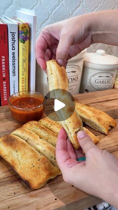 a person is cutting up some bread on a wooden board with sauces and books in the background