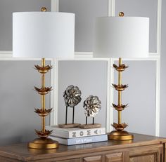 two lamps sitting on top of a wooden table next to a book and lamp shade