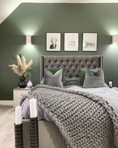 a bedroom with green walls and gray bedding, two framed pictures on the wall