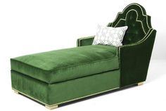 a green velvet chaise lounge chair with gold trimmings and a decorative pillow