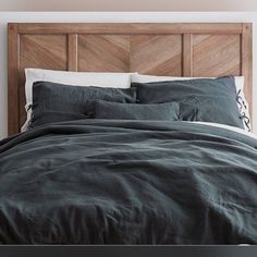 an unmade bed with dark green linens and wooden headboard in a white room