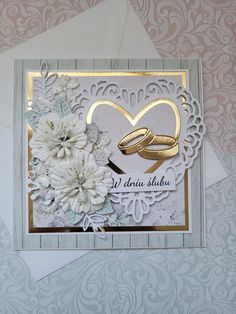 a wedding card with two gold rings and white flowers on the front, surrounded by envelopes