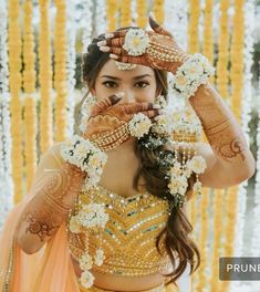 a woman in a yellow dress holding her hands up to her face with flowers around her neck