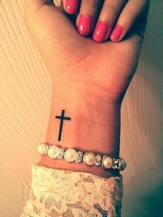 a woman's wrist with a cross tattoo on it and pearls around the wrist