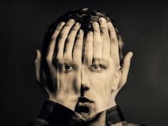 a man covering his face with both hands while standing in front of a black and white photo