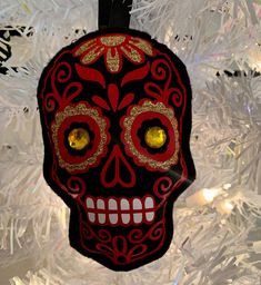 a red and black sugar skull ornament hanging from a christmas tree