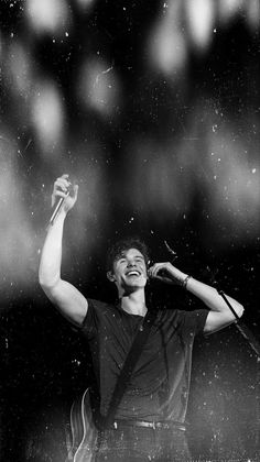 a black and white photo of a man singing into a microphone with his arms in the air