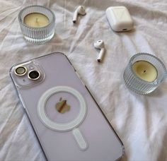 an iphone is sitting on a bed next to some candles and headphones with the cover off