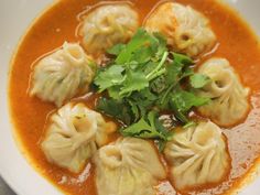 some dumplings are in a red broth with cilantro