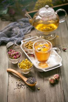 tea and flowers on a wooden table next to a glass teapot with a spoon