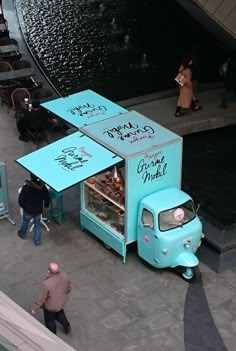 an ice cream truck parked in front of a building with people walking around it and on the sidewalk