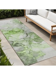 a green rug on the ground in front of a white couch and some plants outside