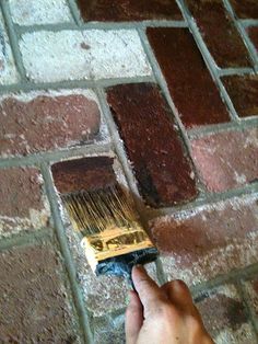 a hand holding a paint brush over a brick wall