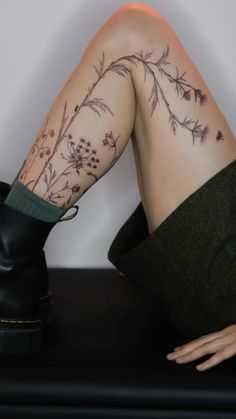 a woman's legs with tattoos and boots on her feet, sitting on a table