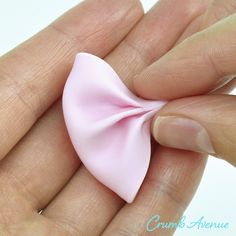 a hand holding a small pink bow in it's palm