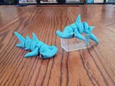 two small blue toy dinosaurs sitting on top of a wooden table next to each other