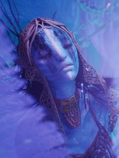 a woman with blue makeup and feathers on her head is looking at something in the distance