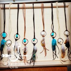 a collection of necklaces with feathers hanging from it's hooks on a wall