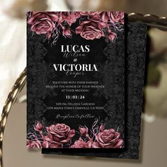 an elegant wedding card with pink roses and black lace is displayed on a table next to flowers