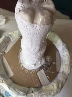 a sculpture made out of toilet paper on top of a wooden plate and covered in plastic wrap