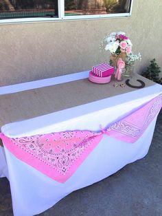 a table with pink and white decorations on it outside next to a window in front of a house