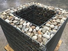 a metal basket filled with rocks sitting on top of a pallet next to a cement floor