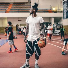 a man holding a basketball while standing on top of a basketball court with other people in the background