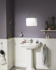 a white pedestal sink in a bathroom with purple walls and shelving on the wall